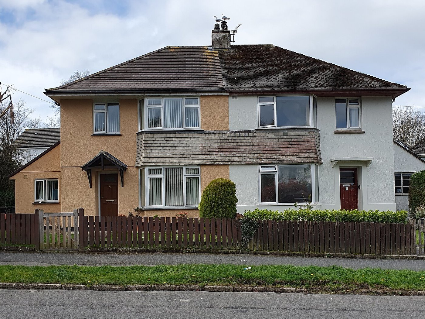 A pair of semi-detached houses with front gardens behind a wooden fence